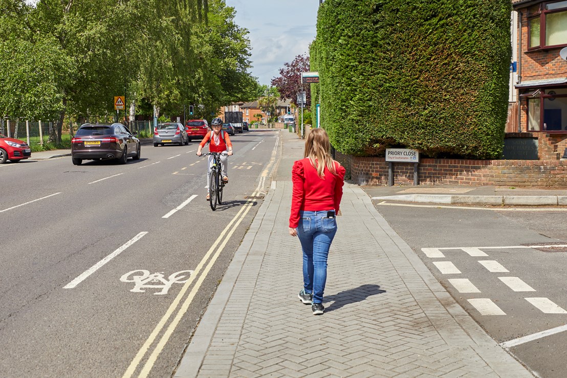 A person walking on a continuous crossing while a person cycling passes in a cycle lane going in the opposite direction