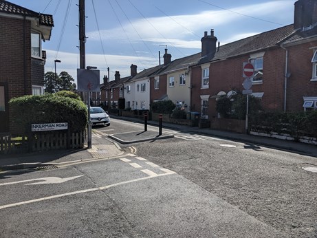 A photo of the carriageway at the junction of Johns Road and Inkerman Road, showing the new pavement area and bollard to reinforce the one way restriction, with houses on Johns Road in the background.